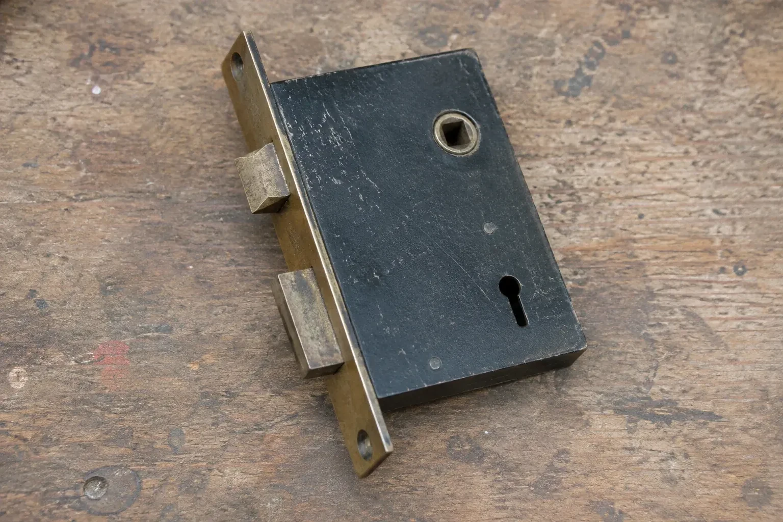 Closed mortise lock case with spindle opening, keyhole, latch and deadbolt on a wooden workbench. — Vintage Mortise Lock Service, Oakville